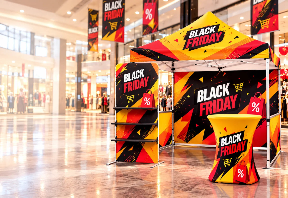 A retail promotional display setup in a shopping mall featuring a pop-up canopy tent, matching side tables, and vertical banner stands printed with bold BLACK FRIDAY graphics in yellow, red, black, and white.